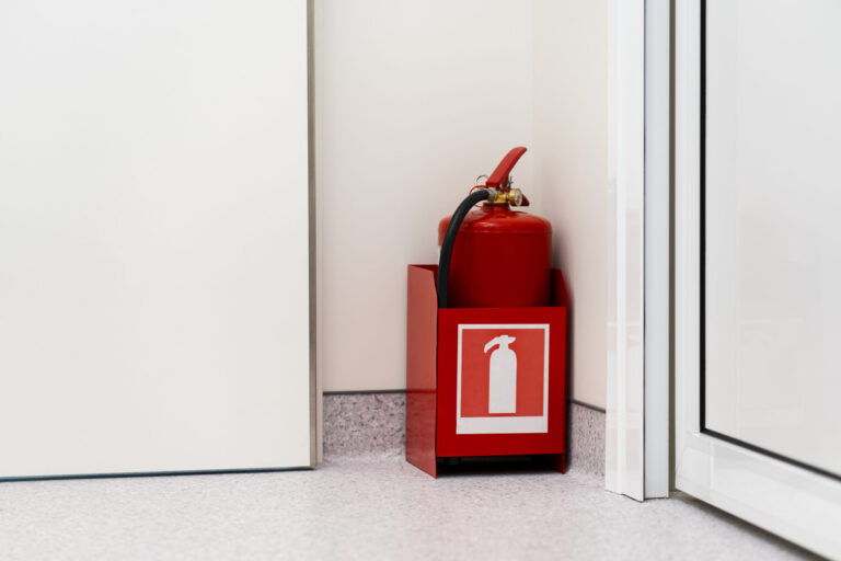 Red fire extinguisher stands in corner, RTek Fire Solutions.